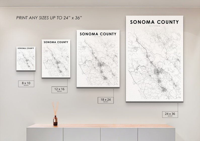 May include: A white wall with four framed maps of Sonoma County, California, in different sizes. The maps are printed in black and white and show the roads and towns of the county. The frames are all white and have a simple design. The text "PRINT ANY SIZES UP TO 24" x 36"" is printed at the top of the wall. The sizes of the maps are 8 x 10 inches, 12 x 16 inches, 18 x 24 inches, and 24 x 36 inches.