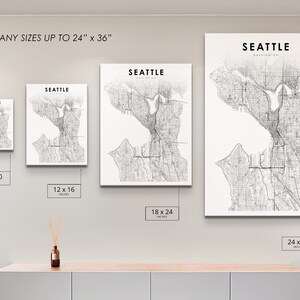 May include: A white wall with four different sized prints of a black and white map of Seattle, Washington. The prints are 8x10 inches, 12x16 inches, 18x24 inches, and 24x36 inches.