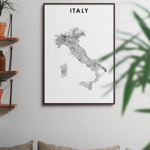 May include: A black and white print of a map of Italy with the word "ITALY" in black text at the top of the print. The print is framed in a black frame and is hanging on a white wall.