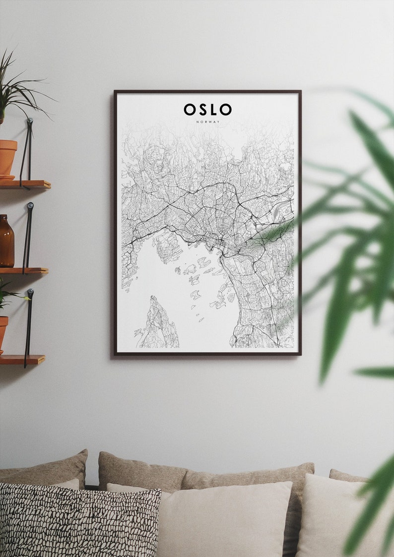 Puede incluir: Un mapa de Oslo, Noruega, en blanco y negro, dibujado con l&iacute;neas, enmarcado en un marco negro y colgado en una pared blanca. El mapa est&aacute; rodeado de plantas y un sof&aacute; con almohadas.