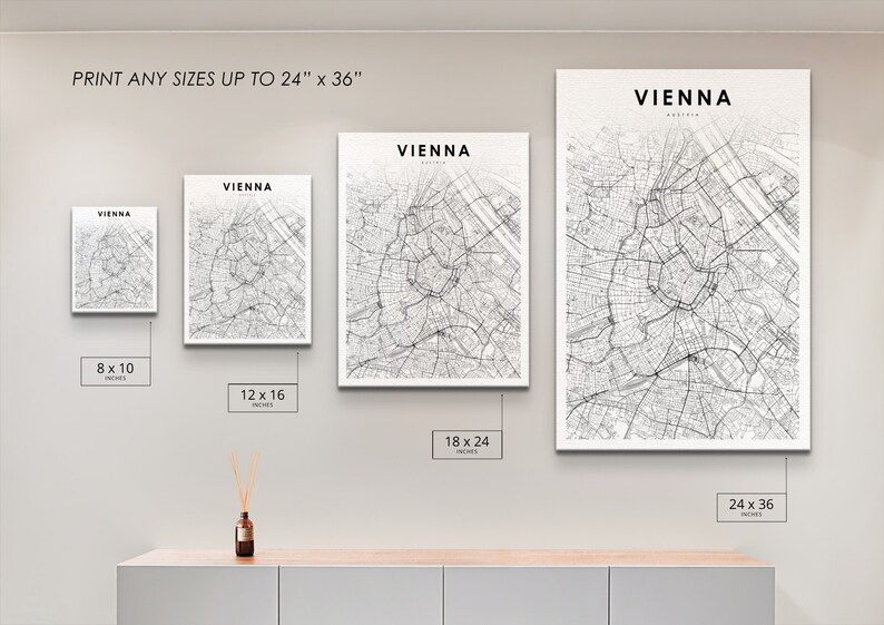 Op de afbeelding: Een witte muur met vier zwart-witte stadskaarten van Wenen, Oostenrijk, in witte lijsten. De kaarten zijn in verschillende formaten: 8 x 10 inch, 12 x 16 inch, 18 x 24 inch en 24 x 36 inch. De tekst "DRUK ALLE FORMATEN TOT 24" x 36" staat bovenaan de muur.