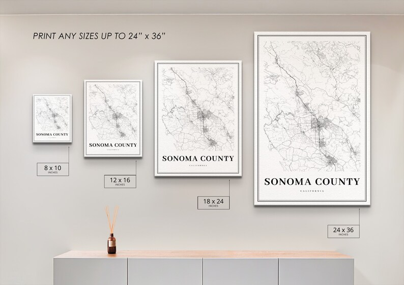 May include: Four different sizes of a black and white map print of Sonoma County, California. The prints are framed in white and are displayed on a light gray wall. The sizes are 8x10 inches, 12x16 inches, 18x24 inches, and 24x36 inches.