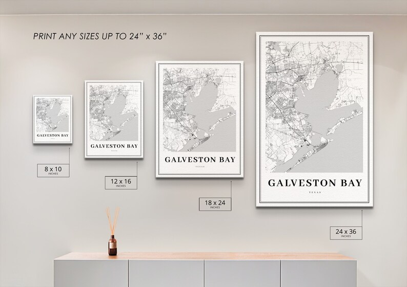 May include: Four different sizes of a black and white map print of Galveston Bay, Texas. The prints are framed in white and displayed on a wall. The sizes are 8x10 inches, 12x16 inches, 18x24 inches, and 24x36 inches.