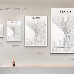 May include: A white wall with four different sized prints of a black and white map of Seattle, Washington. The prints are 8x10 inches, 12x16 inches, 18x24 inches, and 24x36 inches.