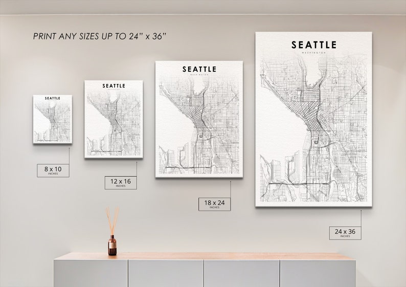 May include: A white wall with four different sized prints of a black and white map of Seattle, Washington. The prints are 8x10 inches, 12x16 inches, 18x24 inches, and 24x36 inches.