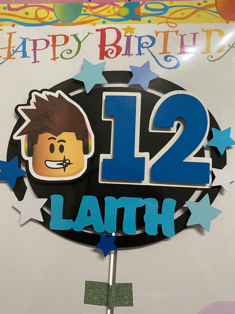 Pode incluir: Um topo de bolo preto e azul com um personagem de desenho animado, o n&uacute;mero 12 e o nome "Lanth". O topo &eacute; decorado com estrelas brancas e azuis.