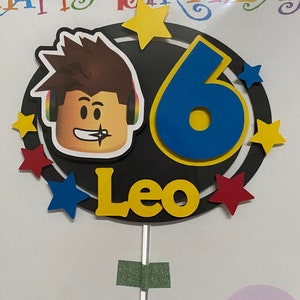 Pode incluir: Um topo de bolo com um personagem Roblox com um n&uacute;mero 6 azul e amarelo, o nome Leo e estrelas amarelas em um fundo preto.
