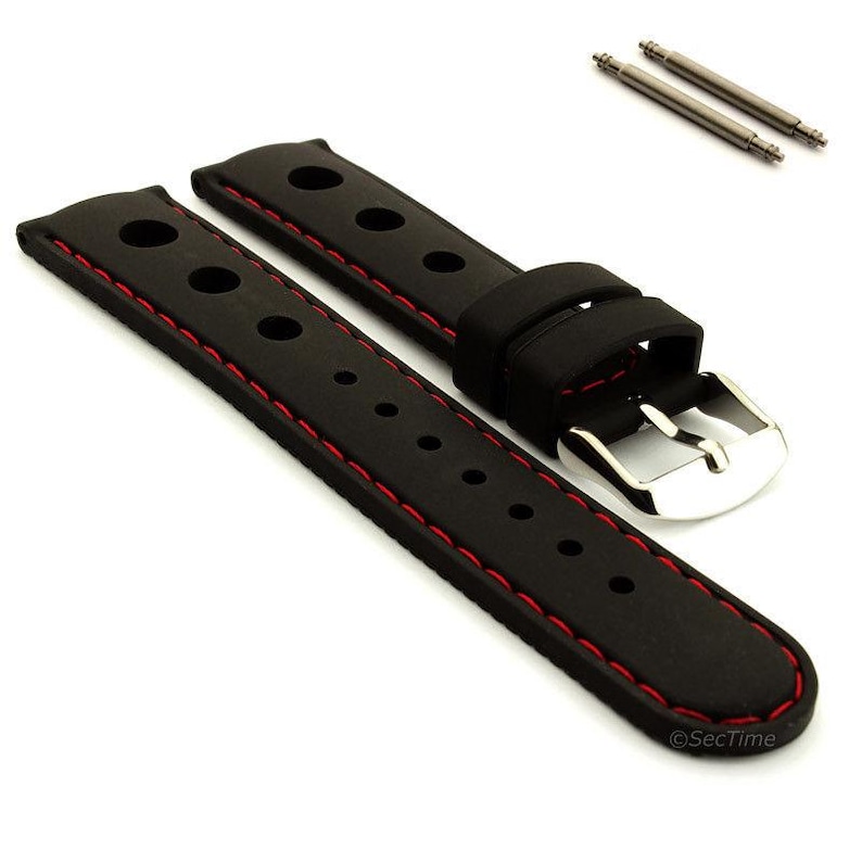 May include: A black rubber watch strap featuring a rally-style design with circular perforations and red contrast stitching along the edges. The strap includes a polished silver-tone metal buckle and two matching metal spring bars for attachment.