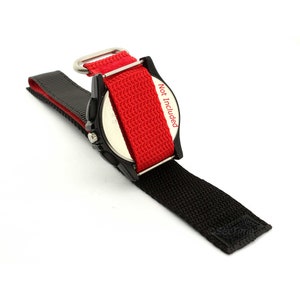 May include: A black watch with a red nylon strap. The strap has a metal buckle and a velcro closure. "Not Included" is written on the strap.