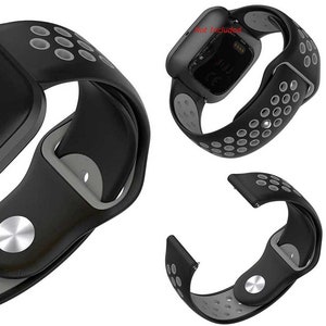 Peut inclure: Bracelet de montre en silicone noir et gris avec un design perfor&eacute;. Le bracelet est compatible avec les montres intelligentes Fitbit Versa 3 et Sense. Le texte "Not Included" est visible sur le cadran de la montre.
