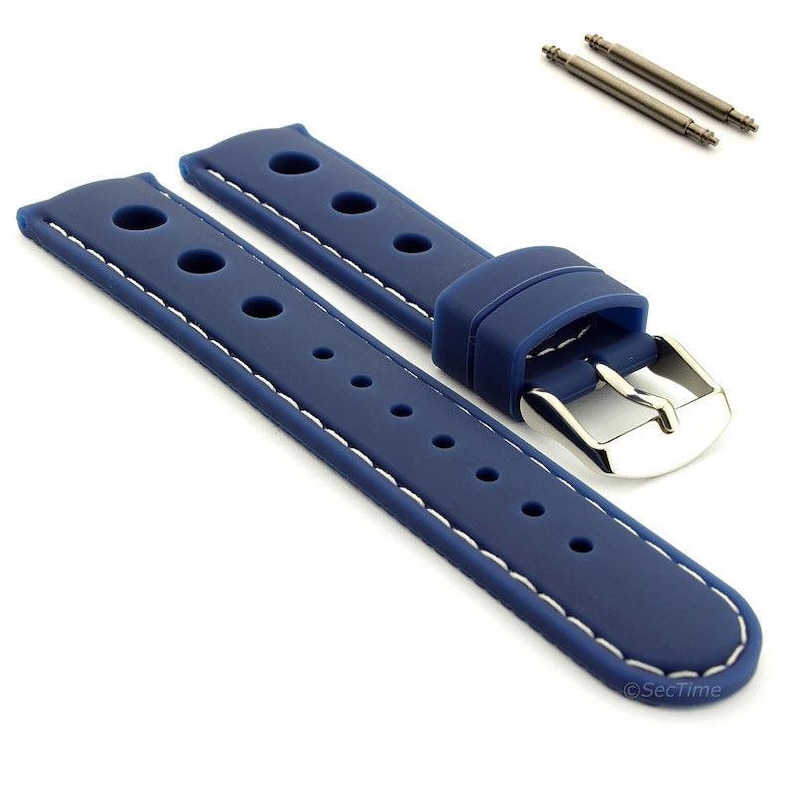 May include: A blue silicone watch strap featuring a perforated design with white contrast stitching, a silver-toned metal buckle, and two matching spring bars. The strap has a smooth texture and multiple adjustment holes along its length.