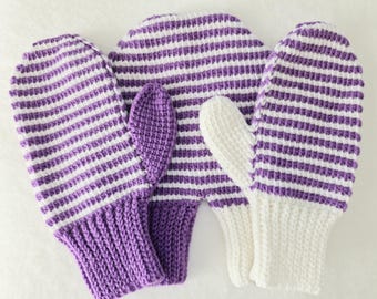 Könnte beinhalten: Handgestrickte Fäustlinge mit lila und weißen Streifen. Die Fäustlinge haben gerippte Bündchen und einen einfarbigen lila Daumen. Der Hauptteil der Fäustlinge weist horizontale Streifen auf. Das Material scheint weiche Wolle zu sein.