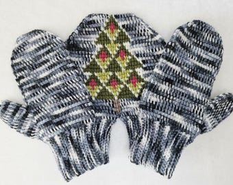 Könnte beinhalten: Handgestrickte Fäustlinge in Grau-, Schwarz- und Weißtönen mit einem Weihnachtsbaum-Motiv. Der Baum ist grün mit rosa Akzenten. Die Fäustlinge sind aus weichem, strukturiertem Garn gefertigt.