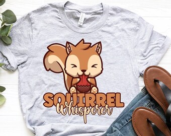 May include: A gray t-shirt with a cartoon squirrel holding an acorn. The text "Squirrel whisperer" is printed below the squirrel.