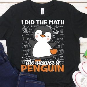 Op de afbeelding: Zwart T-shirt met een witte pinguïn afbeelding en de tekst "Ik heb de wiskunde gedaan, het antwoord is pinguïn".