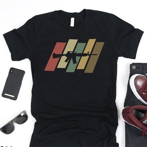 May include: Black t-shirt featuring a retro-style graphic of a rifle on a striped background.