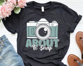 May include: Black t-shirt with a graphic of a vintage camera and the text "About to Snap".