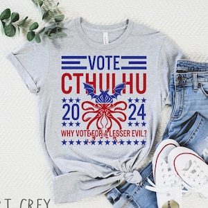 May include: A gray t-shirt with a red, white, and blue graphic design featuring a cartoon Cthulhu with the text "VOTE CTHULHU 2024 WHY VOTE FOR A LESSER EVIL?"