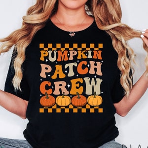 May include: Black t-shirt with a retro-style graphic that says "Pumpkin Patch Crew" with orange and brown pumpkins and a checkered background.