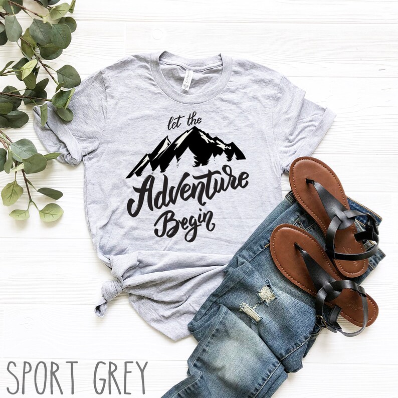 May include: A grey t-shirt with a black mountain graphic and the text "Let the Adventure Begin".