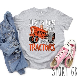 May include: A gray t-shirt with the text "Just a boy who loves tractors" in orange. A cartoon image of a red tractor is in the center of the shirt.