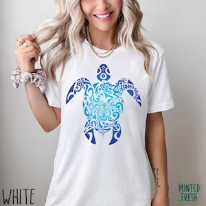 May include: White t-shirt with a blue and white gradient design of a stylized turtle with intricate patterns. The design is centered on the shirt.