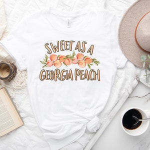 May include: White t-shirt with the text "Sweet as a Georgia Peach" and a graphic of peaches with leaves.