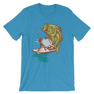 May include: A turquoise blue t-shirt with a graphic of a fisherman in a boat reeling in a large green bass.