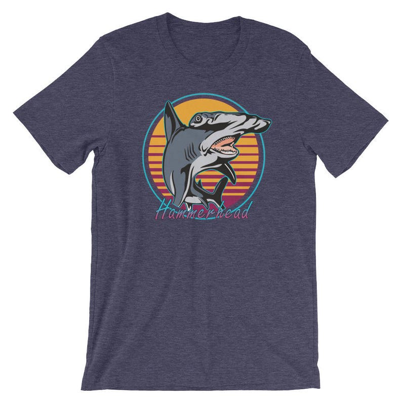 Puede incluir: Una camiseta azul marino con un gr&aacute;fico retro de un tibur&oacute;n martillo en una puesta de sol. El texto "Hammerhead" est&aacute; impreso debajo del tibur&oacute;n.