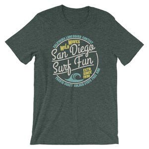 May include: A dark green t-shirt with a vintage-style circular graphic that says "Wild Waves San Diego Surf Fun" with a blue wave graphic and the text "California Longboard Contest Est. Since 1990 Pacific Coast Golden State Free Ride".
