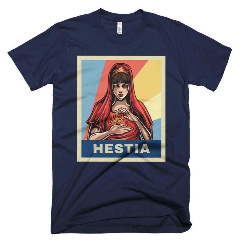 K&ouml;nnte beinhalten: Ein marineblaues T-Shirt mit einem Vintage-Poster-Design, das eine Frau mit roten Haaren und einem roten Gewand zeigt, die eine Flamme in ihren H&auml;nden h&auml;lt. Der Text des Posters lautet "Hestia".