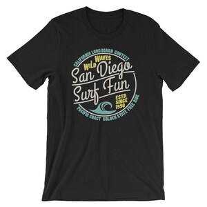 May include: Black t-shirt with a vintage-style graphic design featuring a circle with the text "California Longboard Contest Wild Waves San Diego Surf Fun Est. Since 1990 Pacific Coast Golden State Free Ride".