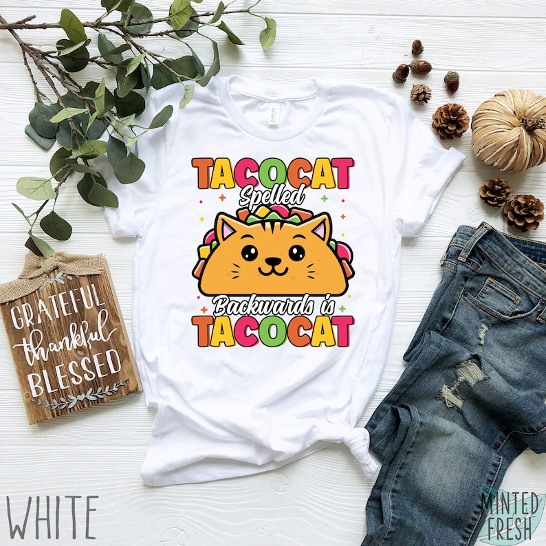 Puede incluir: Camiseta blanca con un gato de dibujos animados en una c&aacute;scara de taco. El texto dice "Tacocat Spelled Backwards is Tacocat".