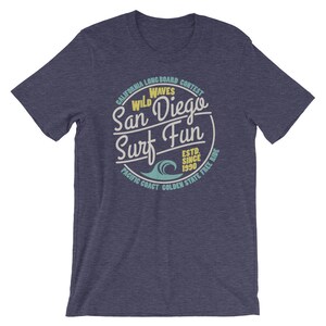 May include: A navy blue t-shirt with a vintage-style graphic of a wave and the text "California Longboard Contest Wild Waves San Diego Surf Fun Est. Since 1990 Pacific Coast Golden State Free Ride".
