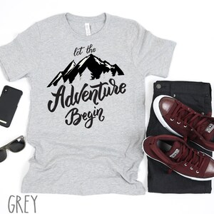 May include: A grey t-shirt with a black mountain graphic and the text "Let the Adventure Begin".