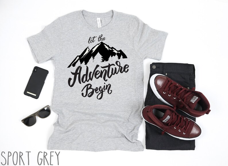 May include: A grey t-shirt with a black mountain graphic and the text "Let the Adventure Begin".