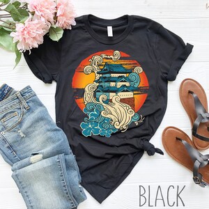 Może przedstawiać: Czarny T-shirt z nadrukiem graficznym japońskiego zamku z falami i kwiatami w k&oacute;łku. Tekst "BLACK" jest nadrukowany na dole obrazu.
