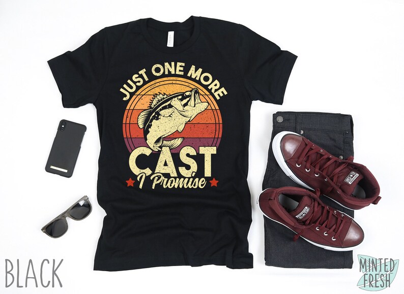 K&ouml;nnte beinhalten: Schwarzes T-Shirt mit einer Grafik im Vintage-Stil eines Fisches, der aus dem Wasser springt. Die Grafik lautet "Just One More Cast I Promise".