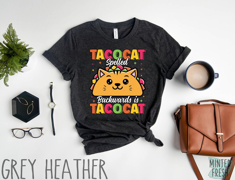 Puede incluir: Una camiseta gris jaspeada oscura con un gato de dibujos animados que lleva un taco. El texto de la camiseta dice "Tacocat Spelled Backwards is Tacocat".