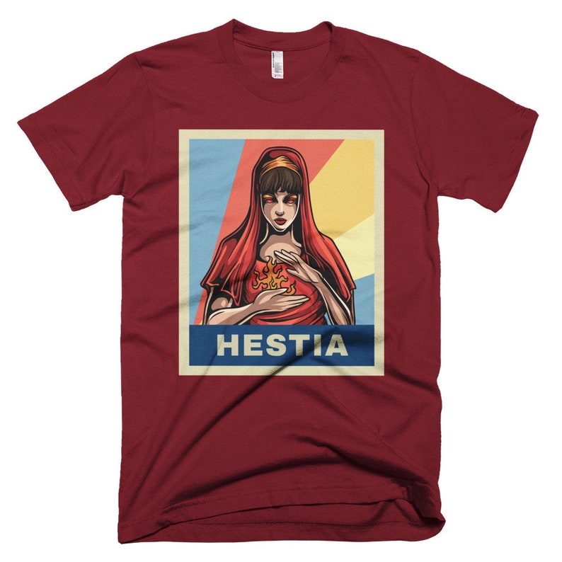 K&ouml;nnte beinhalten: Ein rotes T-Shirt mit einem Vintage-Poster-Design, das eine Frau mit roten Haaren und einem roten Kleid zeigt. Das Poster lautet "Hestia" in blauen Buchstaben.