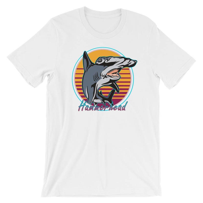 Puede incluir: Camiseta blanca con un gr&aacute;fico retro de un tibur&oacute;n martillo frente a una puesta de sol. El texto "Hammerhead" est&aacute; impreso debajo del tibur&oacute;n.