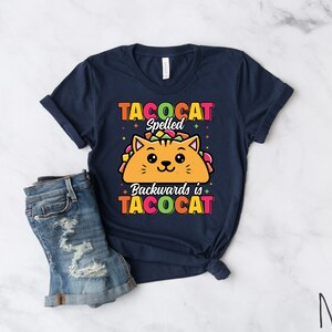 Puede incluir: Una camiseta azul marino con un gato de dibujos animados dentro de un taco. El texto de la camiseta dice "Tacocat Spelled Backwards is Tacocat".