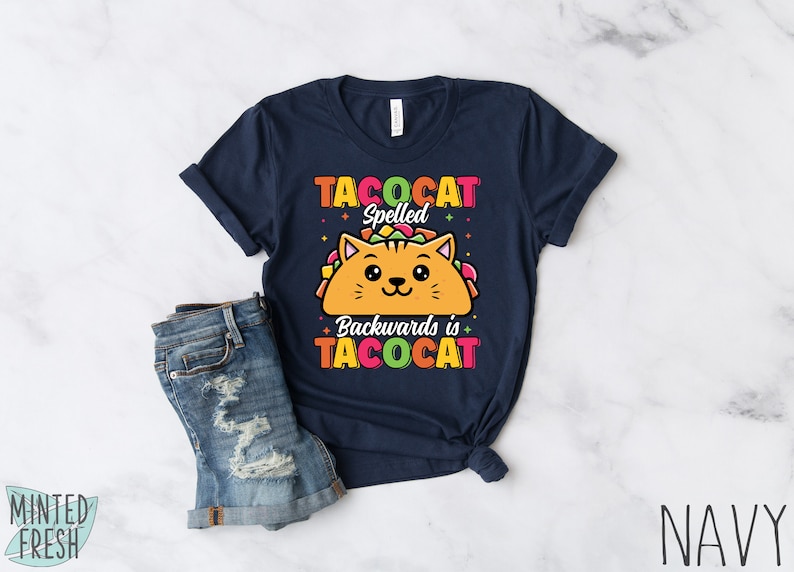 Puede incluir: Una camiseta azul marino con un gato de dibujos animados dentro de un taco. El texto de la camiseta dice "Tacocat Spelled Backwards is Tacocat".