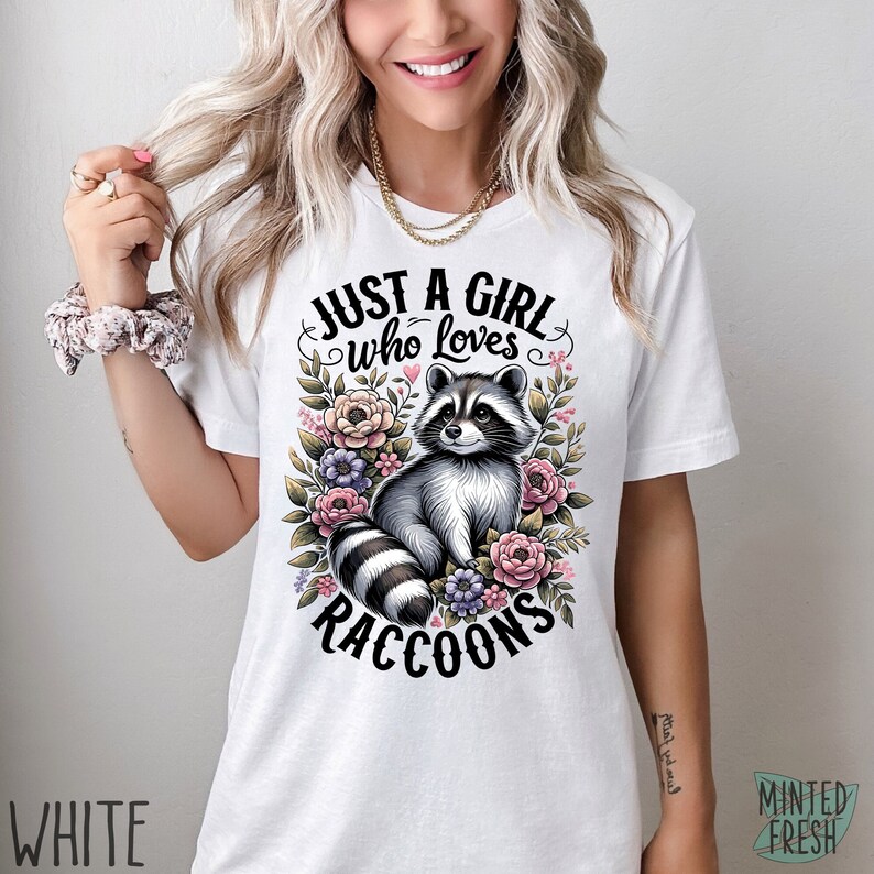 May include: White t-shirt with a graphic of a raccoon surrounded by flowers and the text "Just a girl who loves raccoons".
