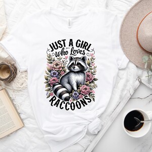 May include: White t-shirt with a graphic of a raccoon surrounded by flowers and the text "Just a girl who loves raccoons".