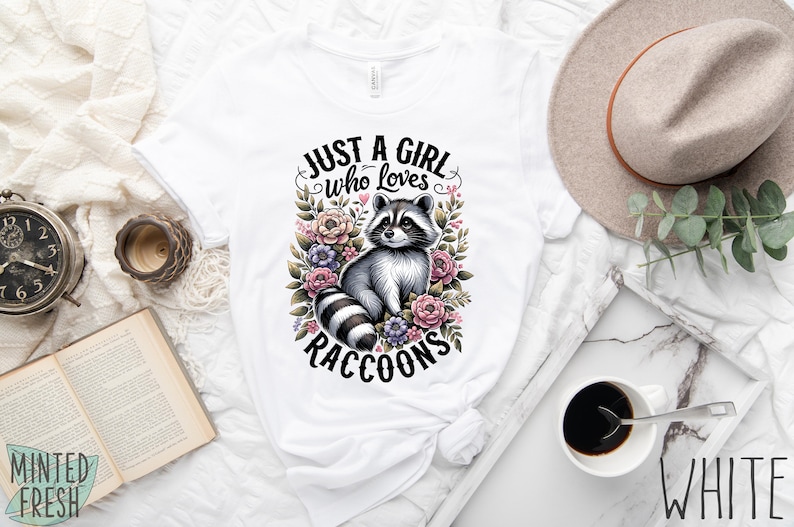 May include: White t-shirt with a graphic of a raccoon surrounded by flowers and the text "Just a girl who loves raccoons".