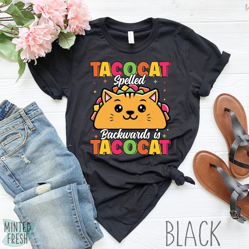 Puede incluir: Camiseta negra con un gato de dibujos animados que lleva un taco. El texto de la camiseta dice "Tacocat Spelled Backwards is Tacocat".