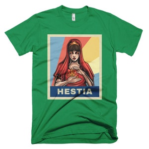 K&ouml;nnte beinhalten: Ein gr&uuml;nes T-Shirt mit einem Vintage-Poster-Design, das eine Frau mit roten Haaren und einem roten Gewand zeigt. Das Poster lautet "Hestia" in fetten wei&szlig;en Buchstaben.