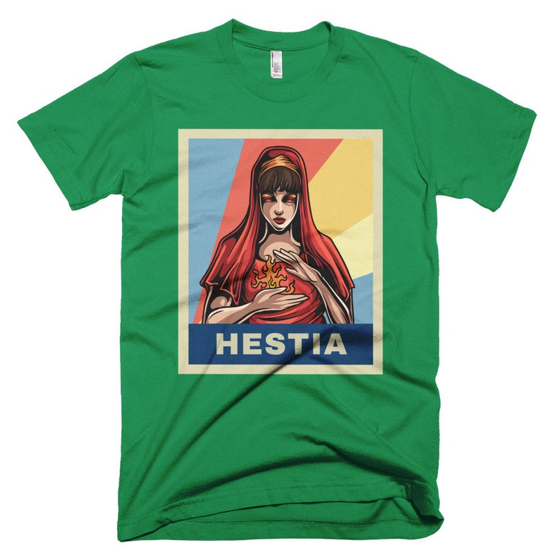 K&ouml;nnte beinhalten: Ein gr&uuml;nes T-Shirt mit einem Vintage-Poster-Design, das eine Frau mit roten Haaren und einem roten Gewand zeigt. Das Poster lautet "Hestia" in fetten wei&szlig;en Buchstaben.