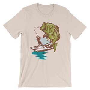 May include: A beige t-shirt with a graphic of a person fishing from a boat with a large bass jumping out of the water.
